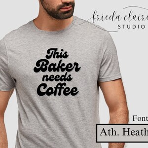 May include: Athletic heather gray t-shirt with the text "This Baker needs Coffee" in a bold, black, retro font. The shirt is a crew neck style. The image also includes the text "Font 29." and "Ath. Heather."