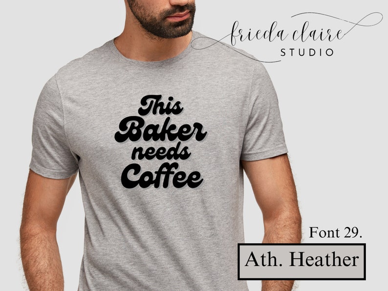 May include: Athletic heather gray t-shirt with the text "This Baker needs Coffee" in a bold, black, retro font. The shirt is a crew neck style. The image also includes the text "Font 29." and "Ath. Heather."