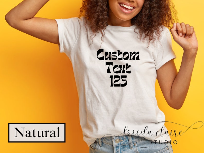 May include: A white t-shirt with the words "Custom Text 123" in black, displayed in a bold, retro font. The shirt is worn by a person with curly hair, against a yellow background. The word "Natural" is in a black box.