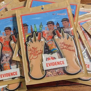May include: A stack of brown paper bags with clear plastic windows, each containing a sticker of a cartoon foot with the words "No More Toe Jam" and "Evidence".