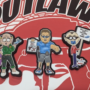 Op de afbeelding: Drie geborduurde patches met cartoonfiguren. De eerste patch toont een vrouw met roze haar en groene kleding die een paarse tas vasthoudt met het woord "DILDOOS" erop. De tweede patch toont een man met een blauw shirt en zwarte shorts die een bord vasthoudt met de tekst "NEW ATF 1934-1986 LAWZ". De derde patch toont een man met een rood shirt en zwarte broek die een bord vasthoudt met de tekst "WILL RIOT FOR TEACHER PAY MMMK".