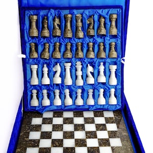 May include: A chess set in a blue velvet case. The chess pieces are two-toned, with dark brown and white pieces. The chessboard has a chequered pattern of white and brown squares. The case is open, displaying the pieces and board.