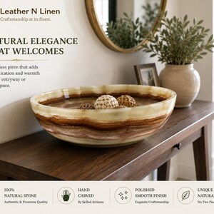 The decorative stone bowl filled with woven spheres rests on a dark wooden entryway console table beneath a round mirror and potted plant.