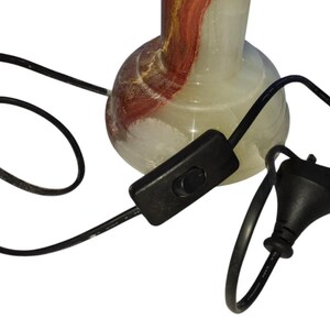 May include: A decorative lamp base with a bulbous shape, featuring a mix of white, red, and brown colors. The lamp has a black cord with an inline switch and a plug.
