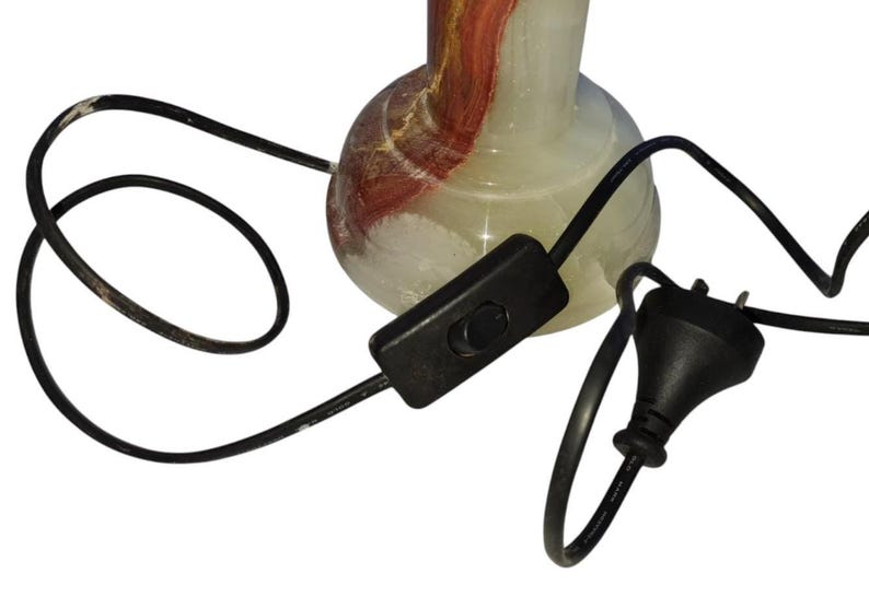 May include: A decorative lamp base with a bulbous shape, featuring a mix of white, red, and brown colors. The lamp has a black cord with an inline switch and a plug.