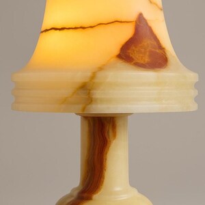 May include: A small, decorative lamp with a cream-colored base and a flared shade. The shade and base feature natural brown and cream veining. The lamp's shade is illuminated, creating a warm, inviting glow. The lamp is a unique home decor item.