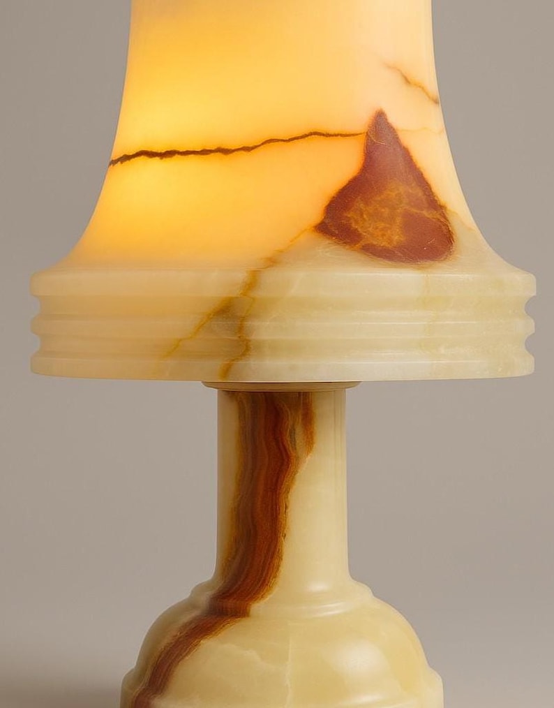 May include: A small, decorative lamp with a cream-colored base and a flared shade. The shade and base feature natural brown and cream veining. The lamp's shade is illuminated, creating a warm, inviting glow. The lamp is a unique home decor item.