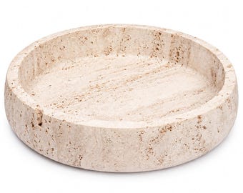 May include: A circular tray crafted from beige travertine stone, featuring a porous, textured surface with natural veining and a shallow, recessed center with thick, rounded walls, presented against a plain white background.