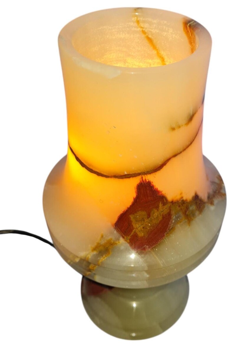 May include: A lit onyx lamp with a warm glow. The lamp has a bulbous base and a cylindrical top, with natural brown and red veining. The lamp is plugged in and ready to use.