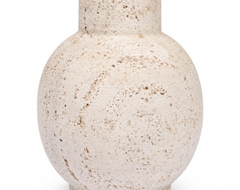 Puede incluir: Un jarrón esférico hecho de piedra beige porosa con una superficie texturizada y picada. El recipiente presenta un cuello cilíndrico y un cuerpo ancho y redondeado, mostrando el aspecto natural e irregular del material claro en bruto.