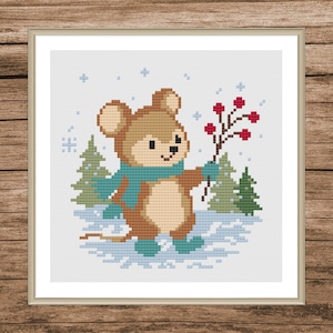 May include: Cross-stitch design of a smiling mouse in a winter scene. The mouse wears a teal scarf and boots, holding a branch with red berries. Snowflakes and evergreen trees are in the background. The artwork is framed.