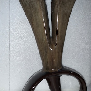 May include: A ceramic vase with a unique design. The vase is brown and has a glossy finish. The vase has two openings at the top and a curved base.