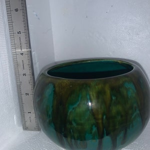 May include: A round, green ceramic planter with brown and green glaze. The planter has a glossy finish and a slightly uneven surface.