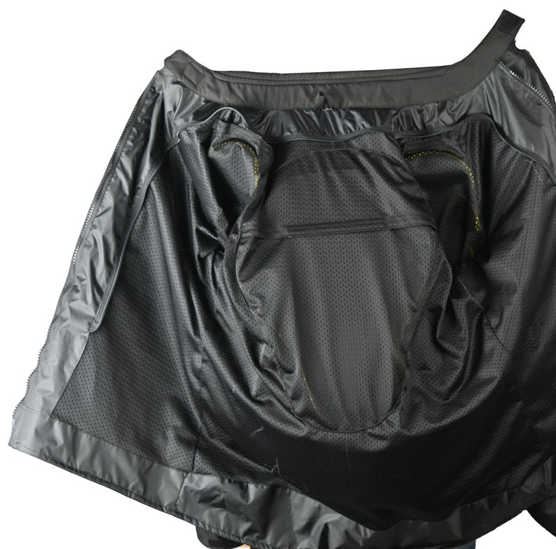 May include: Black motorcycle jacket interior with a mesh lining and multiple pockets. The jacket is open, revealing the inside construction and design. The interior features a zippered pocket and a breathable mesh material.