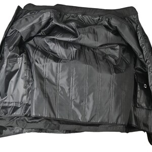 May include: Black jacket with an open design, showcasing the interior lining. The inside features multiple pockets and a quilted pattern. The jacket is made of a shiny, water-resistant material, suitable for outdoor wear.