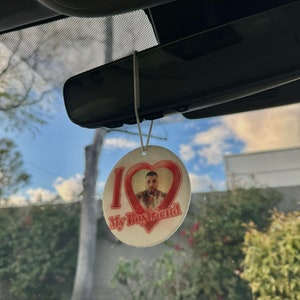 May include: A white car air freshener with a red heart and the text "I love my boyfriend". A man's face is visible inside the heart.
