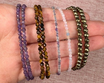 May include: Six beaded bracelets in various colors, including purple, brown, blue, pink, and gold. The bracelets are made of small, faceted beads.