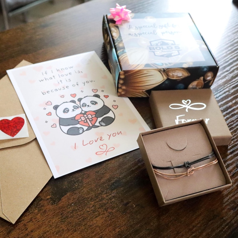 以下が含まれることがあります： 2匹のパンダと「If I know what love is, it is because of you. I Love you」という文字が書かれたグリーティングカード、白い無限大のシンボルと「Forever」という文字が書かれた茶色の箱、そして2本の細いコードブレスレットが入ったギフトセット。