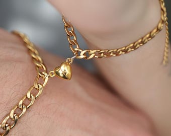 May include: Gold-colored chain bracelets with a heart-shaped charm. The bracelets are connected by a magnetic clasp, creating a matching set. The chains have a curb link design, and the heart charm is a solid gold color.