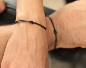 以下が含まれることがあります： 黒いコードブレスレット、結び目デザイン。 ブレスレットはシンプルでミニマリストで、日常使いに適しています。 ブレスレットは2つの手首に表示されています。