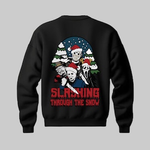 May include: Black sweatshirt with a Christmas-themed design featuring horror movie characters wearing Santa hats. The text "SLASHING THROUGH THE SNOW" is printed below the image.