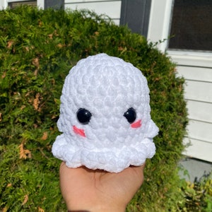 May include: A white crocheted ghost with black eyes and pink cheeks. The ghost is holding a small white crocheted heart.