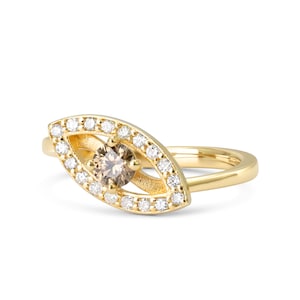 May include: A gold ring with a brown diamond set in a halo of smaller diamonds. The ring is shaped like an eye.