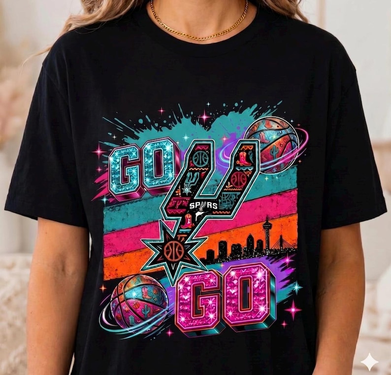 Może przedstawiać: Czarny t-shirt z nadrukiem graficznym z napisem GO GO. Projekt zawiera stylizowane logo Spurs, piłki do koszyk&oacute;wki z motywami westernowymi, sylwetkę panoramy miasta oraz kolorowe poziome paski w odcieniach turkusu, r&oacute;żu i pomarańczu.