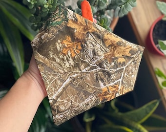 May include: A camouflage bandana with a brown, green, and white pattern. The bandana has the text "MOOSE EDGE" printed on it.