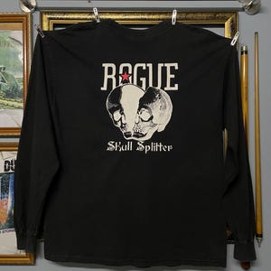 Könnte beinhalten: Schwarzes Langarmshirt mit dem Wort "ROGUE" über einer Grafik eines gespaltenen Schädels. Der Text "Skull Splitter" befindet sich darunter. Das Shirt hängt an einer Wäscheleine.