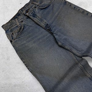May include: Faded blue denim jeans with classic five-pocket styling. The jeans have a button and zipper closure, belt loops, and a worn appearance. The denim is a medium wash with subtle fading and wear marks.