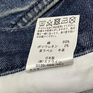 以下が含まれることがあります： デニム生地のクローズアップ。白いタグには洗濯表示と生地組成が表示されています。綿98％、ポリウレタン2％、革ラベル。タグのテキストは日本語です。