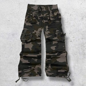 Peut inclure: Pantalon cargo camouflage dans les tons de vert, marron et gris. Le pantalon comporte plusieurs poches avec fermetures à rabat et des sangles réglables. Des cordons de serrage sont visibles aux chevilles. Un design d'inspiration militaire classique.