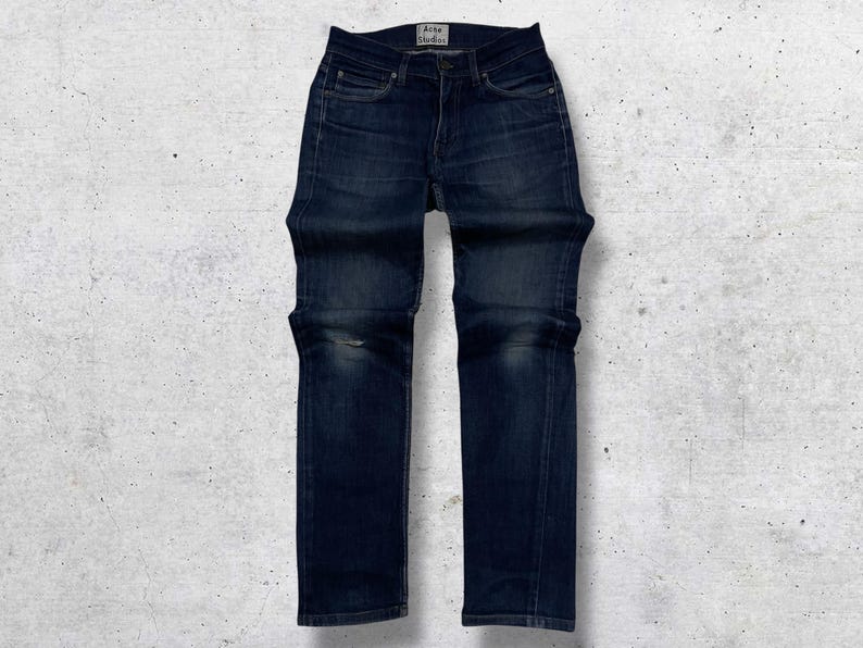 Op de afbeelding: Donkerblauwe denim jeans met een klassiek vijf-zakken ontwerp. De jeans hebben een rechte pijp en een vervaagde uitstraling, met subtiele slijtage op de knie&euml;n. De merknaam "Acne Studios" is zichtbaar op de tailleband.