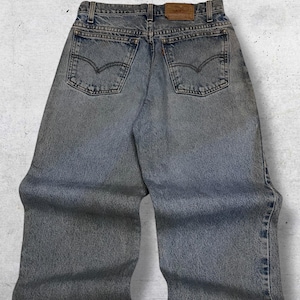 May include: Light blue denim jeans with the Levi's brand label on the back. The jeans have a classic five-pocket design, with the Levi's logo on the back pockets. The jeans are faded and have a worn look.