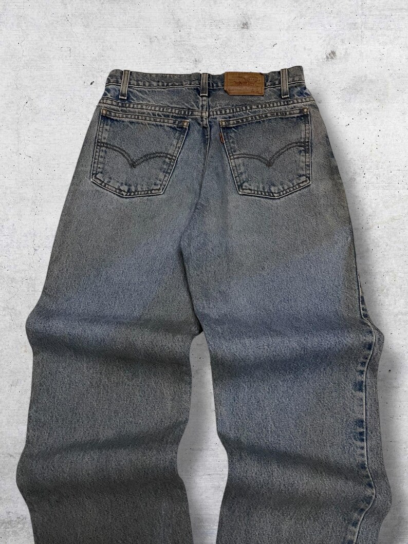 May include: Light blue denim jeans with the Levi's brand label on the back. The jeans have a classic five-pocket design, with the Levi's logo on the back pockets. The jeans are faded and have a worn look.