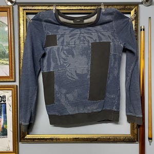 May include: A blue and gray Diesel sweatshirt with a patchwork design. The sweatshirt features a crew neck, long sleeves, and the word "DIESEL" printed on the sleeve. The design includes a tiger print.