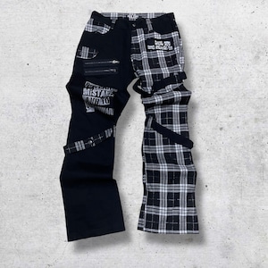 May include: Black and white plaid and solid black pants with zippers, straps, and text. The left leg is solid black with zippers and text that reads "MISTAKE AND WAR". The right leg is black and white plaid.