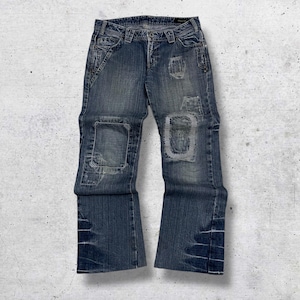 May include: Blue denim jeans with distressed patches on the knees and thighs. The jeans have a low-rise waist and a flared leg opening. The jeans have a button and zipper closure and pockets on the front and back.