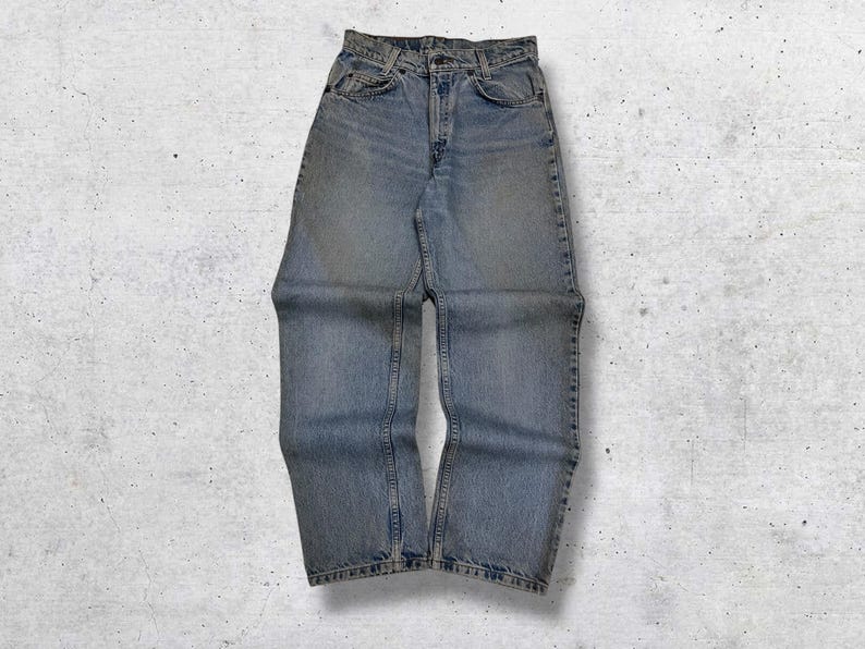 May include: Light blue denim jeans with a classic five-pocket design. The jeans have a faded wash and a straight leg cut. The waist is buttoned and the jeans are laid flat on a textured surface.