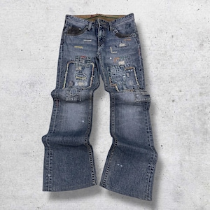 Könnte beinhalten: Blaue Jeans mit Patchwork-Details. Die Jeans hat eine verwaschene Optik, ein klassisches Fünf-Taschen-Design und ein ausgestelltes Bein. Auf der Vorderseite sind Flicken in verschiedenen Größen und Texturen aufgenäht, was für visuelles Interesse sorgt.