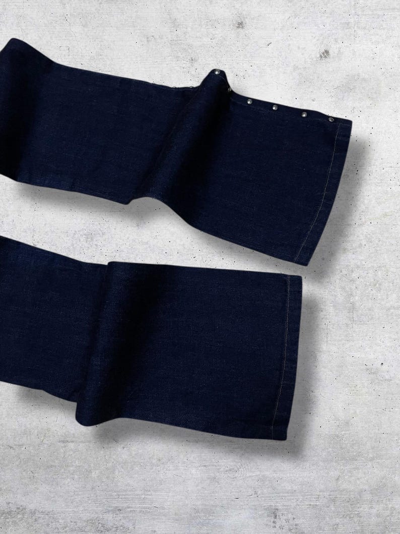Puede incluir: Pantalones vaqueros azul marino oscuro con dise&ntilde;o de pernera ancha. Los pantalones tienen una serie de peque&ntilde;os remaches plateados a lo largo del borde superior de la cintura doblada. La tela parece ser un denim de peso medio.