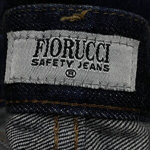 Puede incluir: Primer plano de una prenda de mezclilla azul oscuro, que muestra una etiqueta que dice "FIORUCCI SAFETY JEANS" en texto negro sobre un fondo gris claro. La etiqueta est&aacute; cosida a la mezclilla.