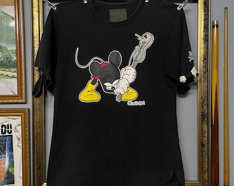 Peut inclure: T-shirt noir avec un dessin de Mickey Mouse tenant une clé. Le graphisme comprend des chaussures jaunes, des gants blancs et un nœud papillon rouge. Le texte "Classic!" est imprimé en dessous du personnage.
