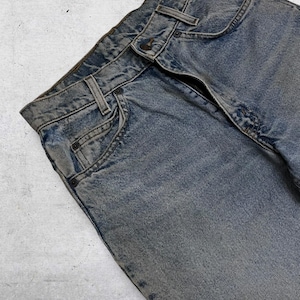 May include: Close-up of faded blue denim jeans. The jeans have a button closure, belt loops, and classic five-pocket styling. The denim has a worn, textured appearance, with subtle variations in color.