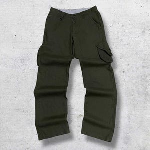 May include: Dark green cargo pants with two large side pockets and a button and zipper closure. The pants are made of a durable fabric and have a relaxed fit. The pants are laid flat on a textured surface.