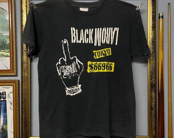 May include: Black t-shirt with a graphic of a hand giving the middle finger, the text "BLACK WOVVI" above it, and "TOKYO" and "$66966" below. The shirt is hanging on a metal bar with clips.