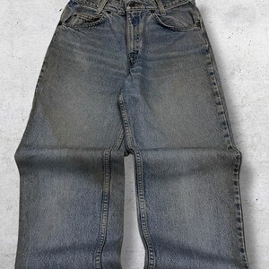 May include: Light blue denim jeans with a classic five-pocket design. The jeans have a faded wash and a straight leg cut. The image shows the jeans laid flat, showcasing the front pockets, button closure, and belt loops. The denim appears worn.