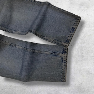 May include: Close-up of a pair of faded blue jeans. The denim pants are folded, showcasing the texture and stitching details. The jeans have a classic five-pocket design and a slightly worn appearance.