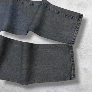 May include: Close-up of folded, dark gray denim jeans. The jeans have a classic five-pocket design with visible stitching and a faded appearance. The fabric appears to be a medium weight denim.